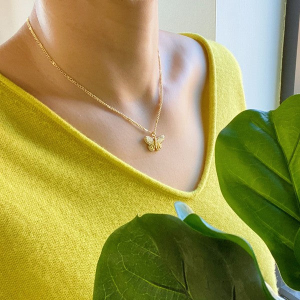 Model wearing Gold Brass Butterfly Charm Necklace standng next to plant leaves