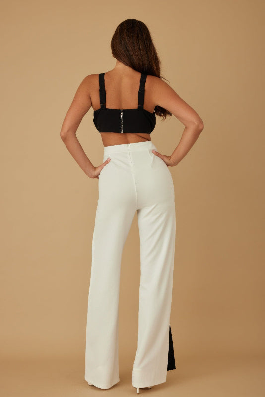 back view of Woman wearing a black top and white pants against a beige background