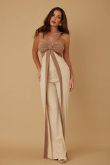 Woman wearing a beige and brown jumpsuit with a bow detail on a beige background
