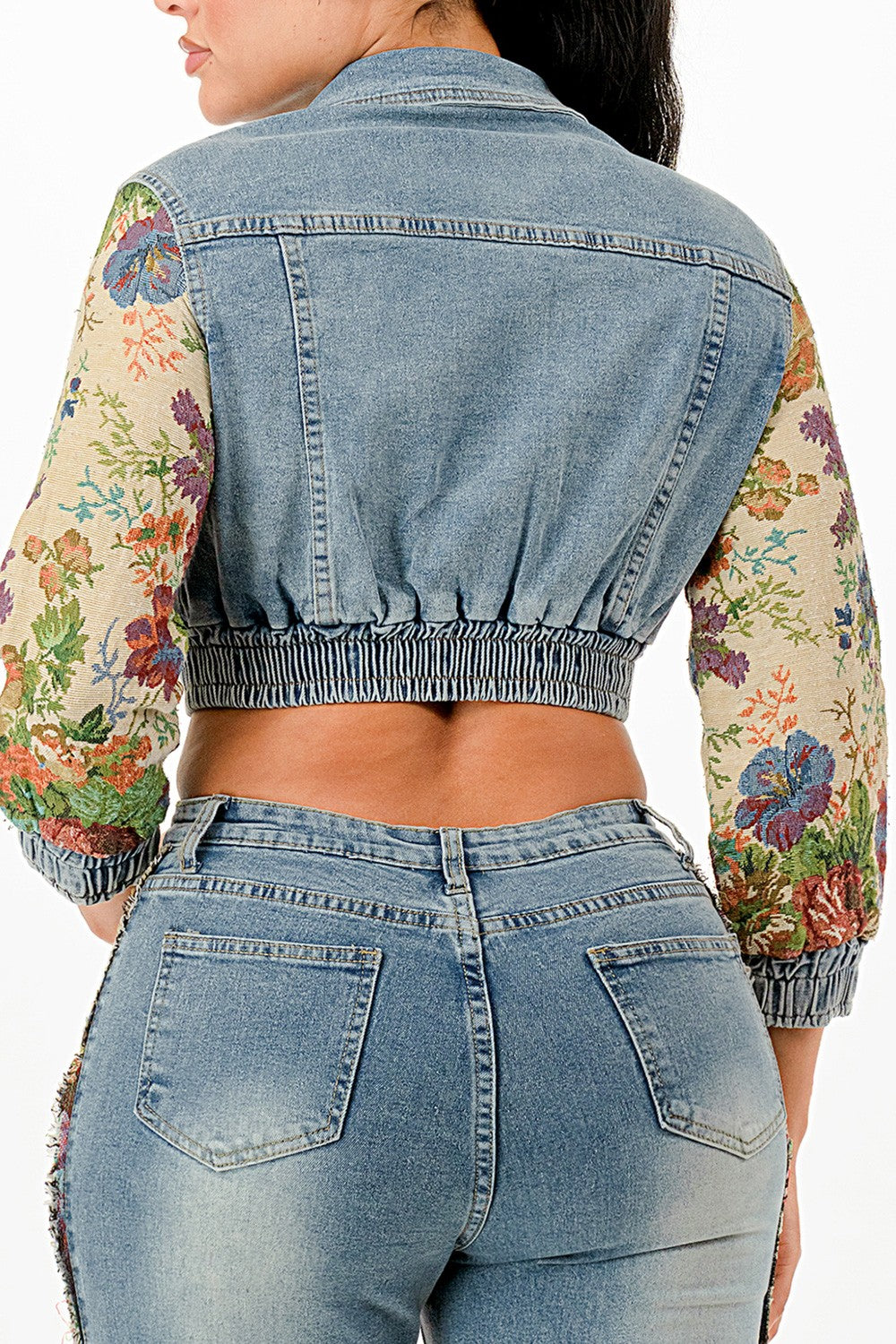 Back view of woman wearing a denim jacket with floral sleeves and matching jeans.
