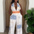 Woman wearing a white patterned jumpsuit standing in front of a plant.