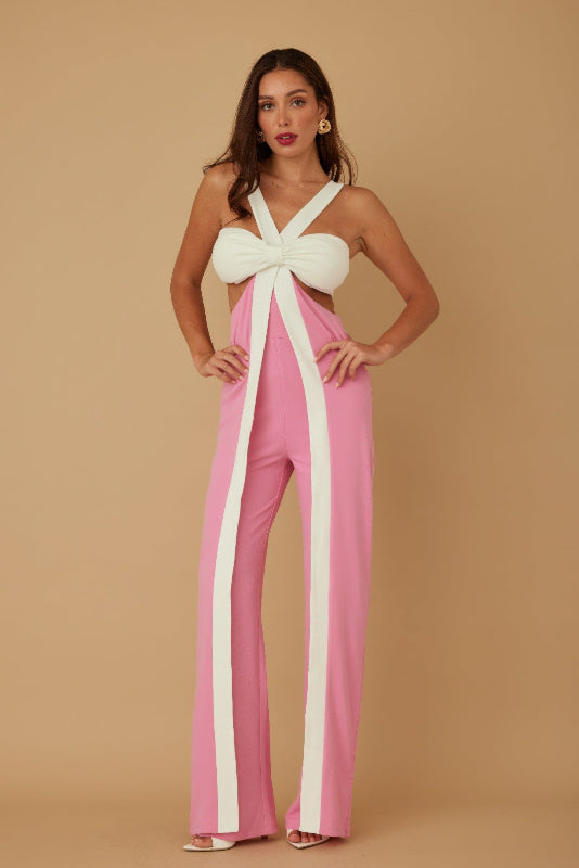 Woman wearing a pink and white jumpsuit with a bow detail on a beige background