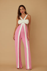 Woman wearing a pink and white jumpsuit with a bow detail on a beige background