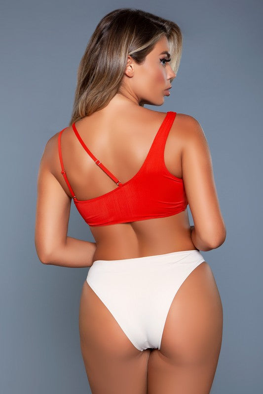 Side view of an asymmetrical two-piece swimsuit with a red one-shoulder top featuring a ring accent and a strappy cutout, paired with high-cut ivory bikini bottoms with a ring detail, showcasing a flattering fit.