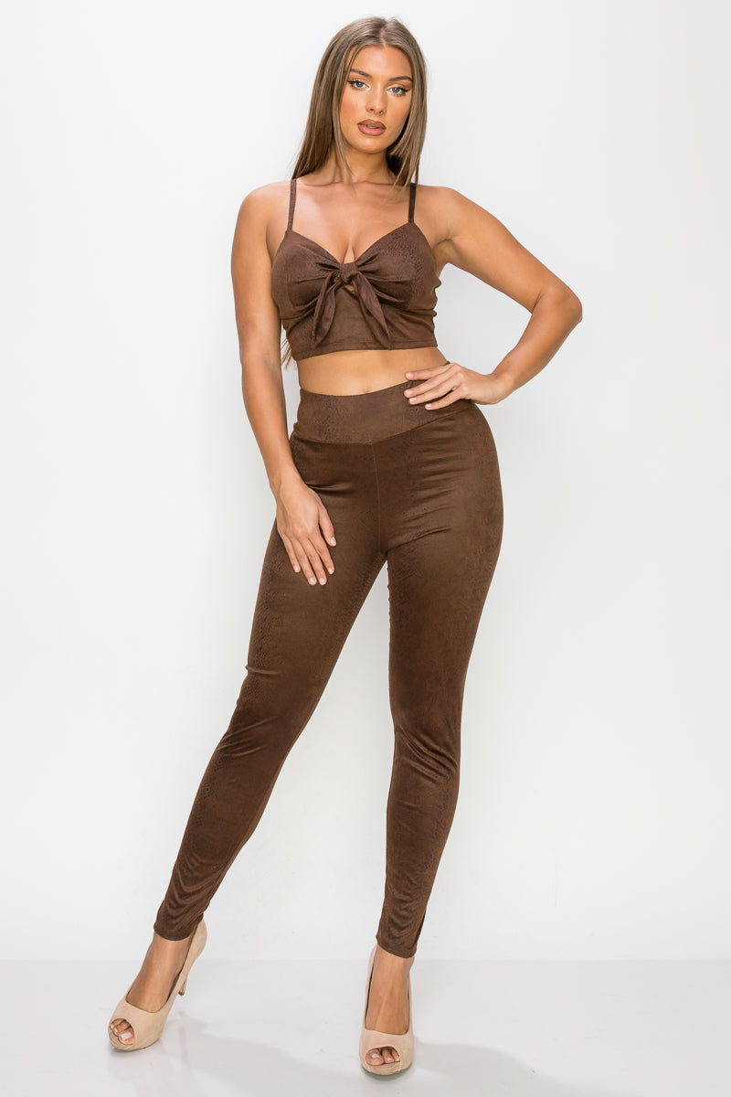 Top: A sleeveless crop top featuring an all-over embossed snake print, front tie, a sweetheart neckline, adjustable cami straps, and a square cut back.  Bottom: A pair of casual skinny leggings featuring an all-over embossed snake print, elasticized high-rise waistband, and a full length. 