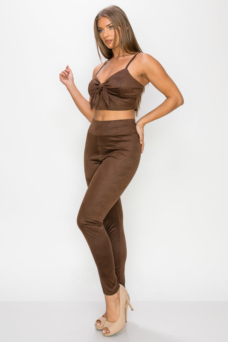 Top: A sleeveless crop top featuring an all-over embossed snake print, front tie, a sweetheart neckline, adjustable cami straps, and a square cut back.  Bottom: A pair of casual skinny leggings featuring an all-over embossed snake print, elasticized high-rise waistband, and a full length. 