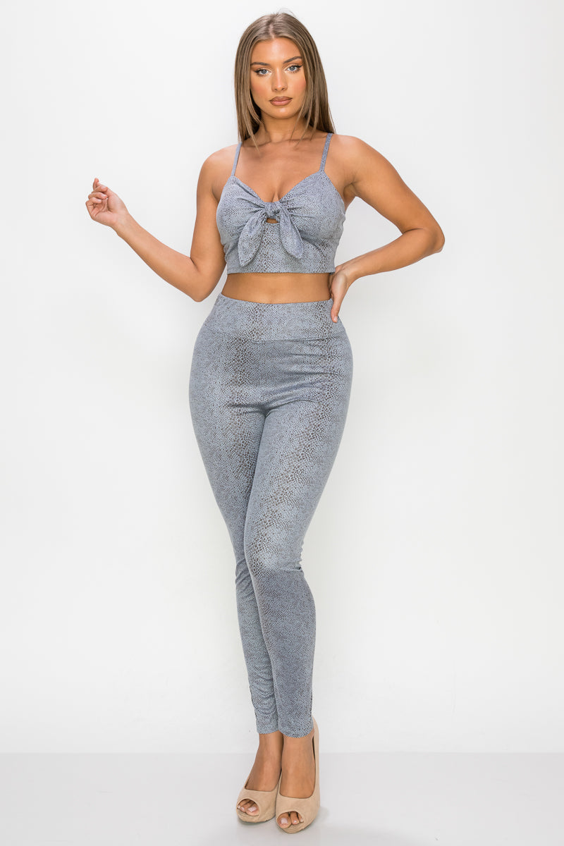 Top: A sleeveless crop top featuring an all-over embossed snake print, front tie, a sweetheart neckline, adjustable cami straps, and a square cut back.  Bottom: A pair of casual skinny leggings featuring an all-over embossed snake print, elasticized high-rise waistband, and a full length. 