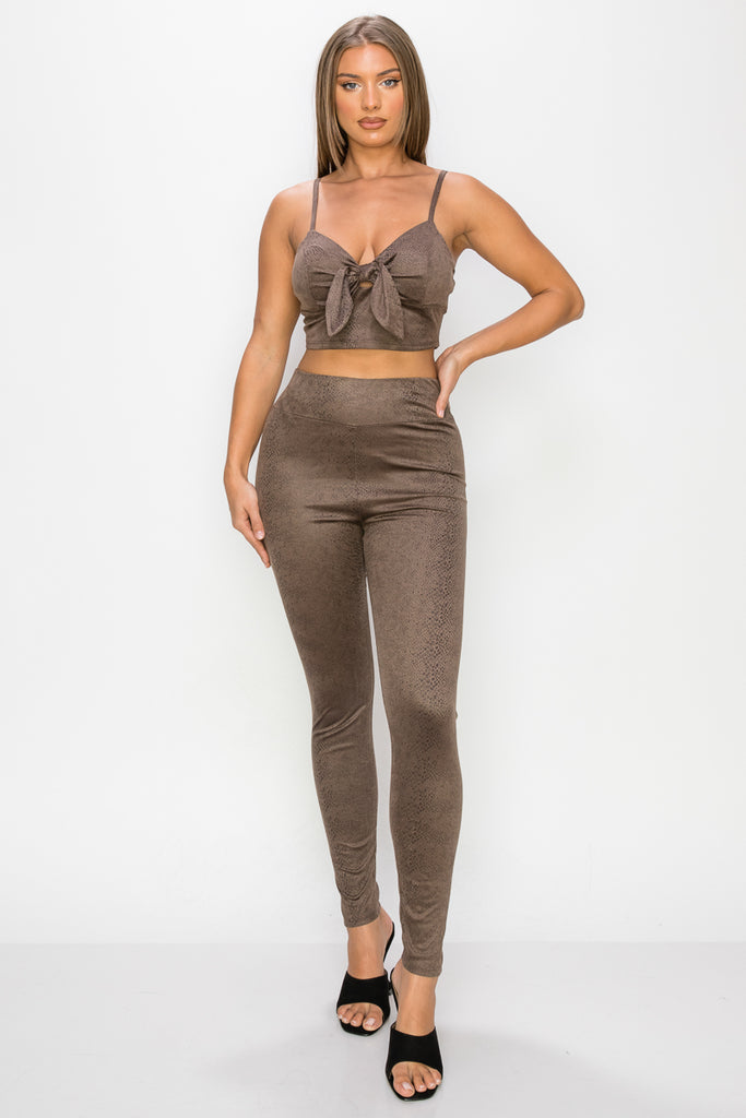 Top: A sleeveless crop top featuring an all-over embossed snake print, front tie, a sweetheart neckline, adjustable cami straps, and a square cut back.  Bottom: A pair of casual skinny leggings featuring an all-over embossed snake print, elasticized high-rise waistband, and a full length. 