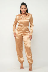 model wearing gold Zip Front Satin Cargo Jogger Jumpsuit with clear heels