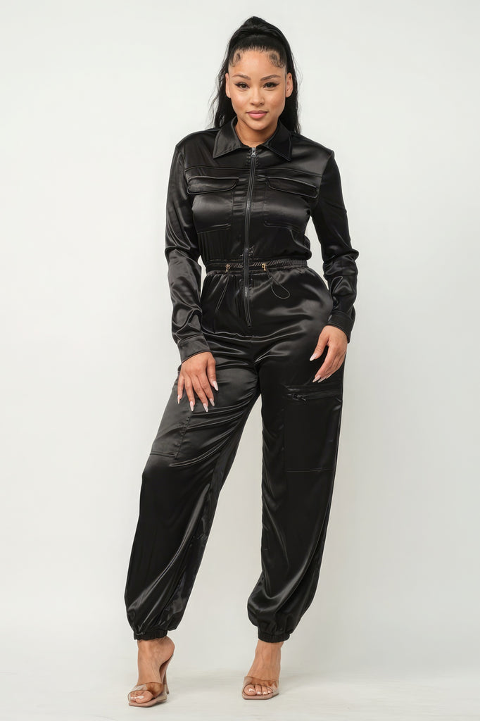 model wearing Black Zip Front Satin Cargo Jogger Jumpsuit with clear heels